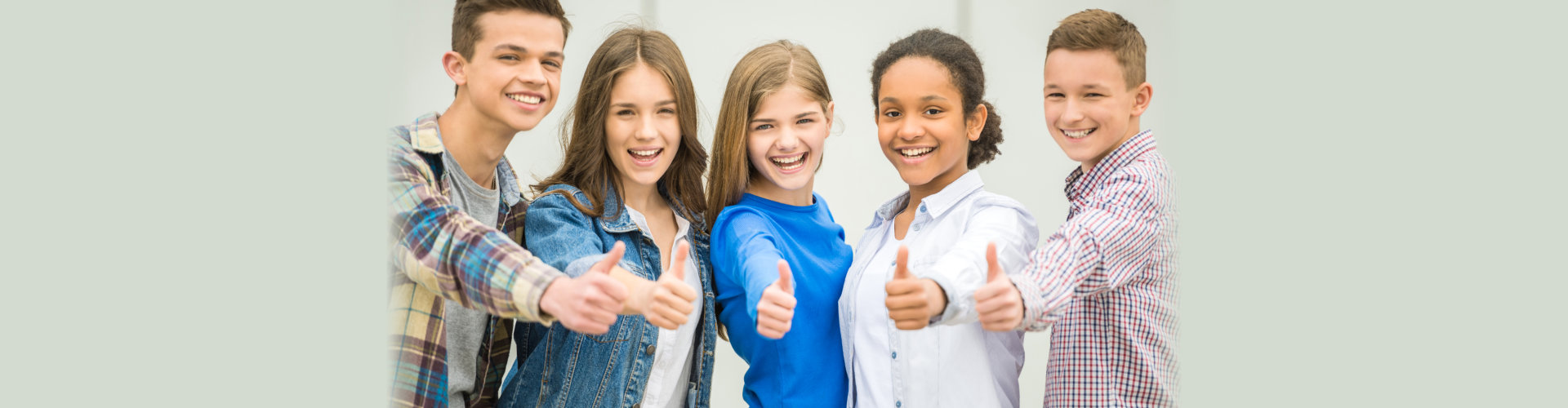 Group of smiling cheerful teenagers having fun after lessons and showing thumbs up